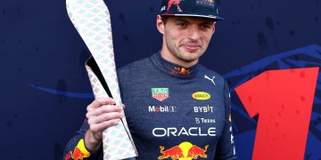 Racing driver holds a unique trophy on podium.