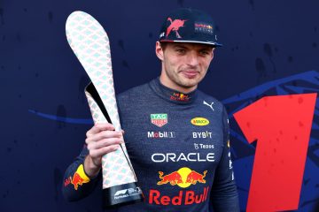Racing driver holds a unique trophy on podium.