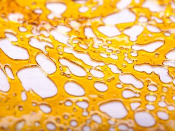 Golden cannabis shatter close-up, translucent texture.