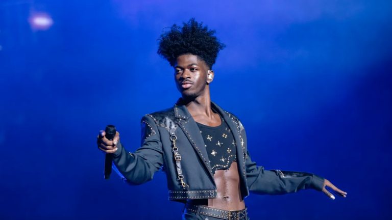 Performer on stage holding microphone, blue background.