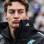 Man in racing jacket pouting at event.