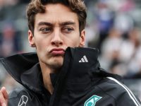 Man in racing jacket pouting at event.