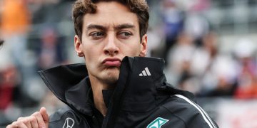 Man in racing jacket pouting at event.