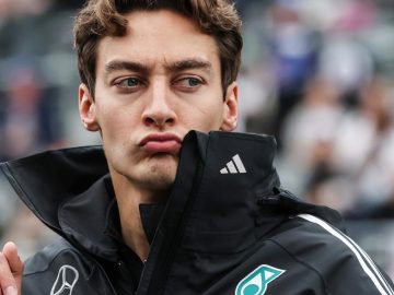 Man in racing jacket pouting at event.