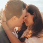 Couple kissing near water during sunset.