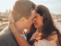 Couple kissing near water during sunset.
