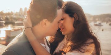 Couple kissing near water during sunset.
