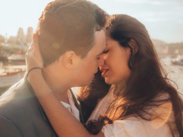 Couple kissing near water during sunset.