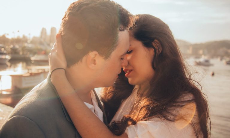 Couple kissing near water during sunset.